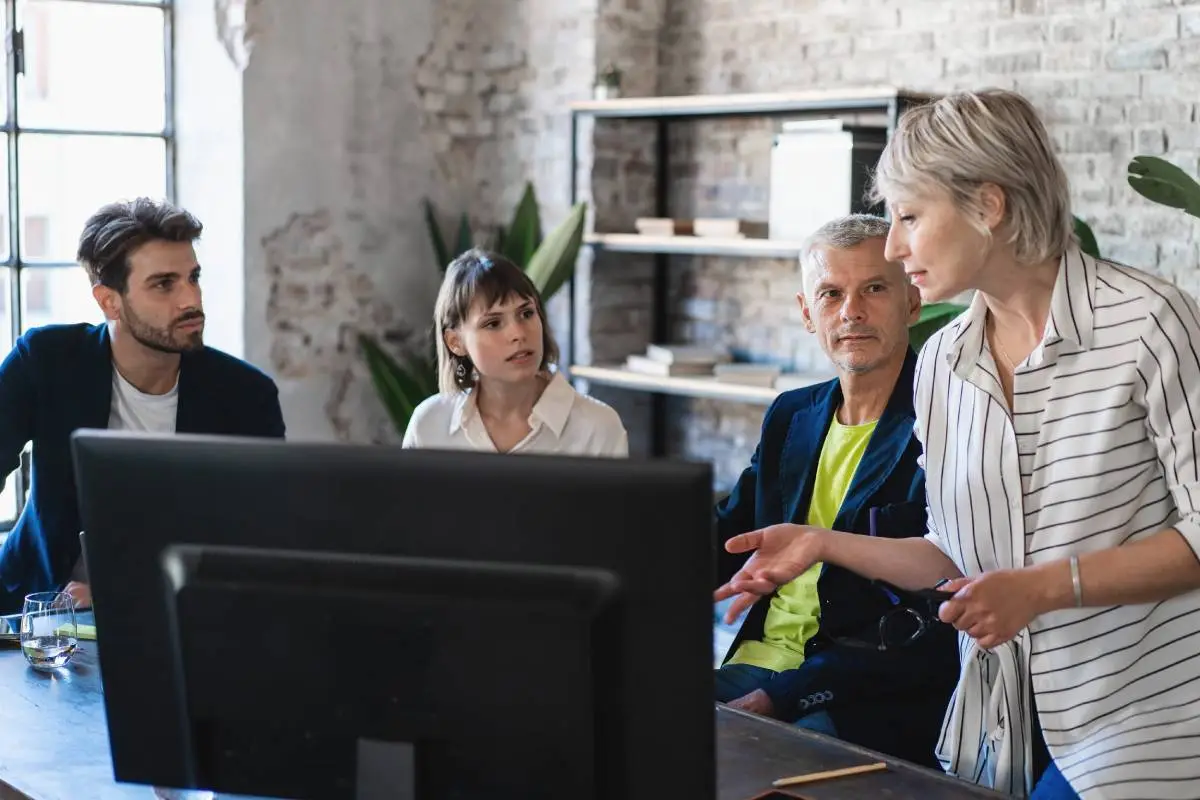four people in an office with three of them sitting and one that is standing up and talking