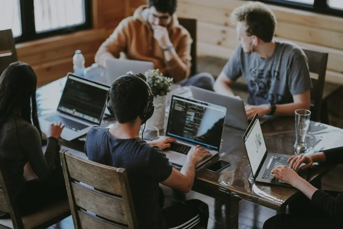 Five people working on a wooden table with their laptop focused and diligently.