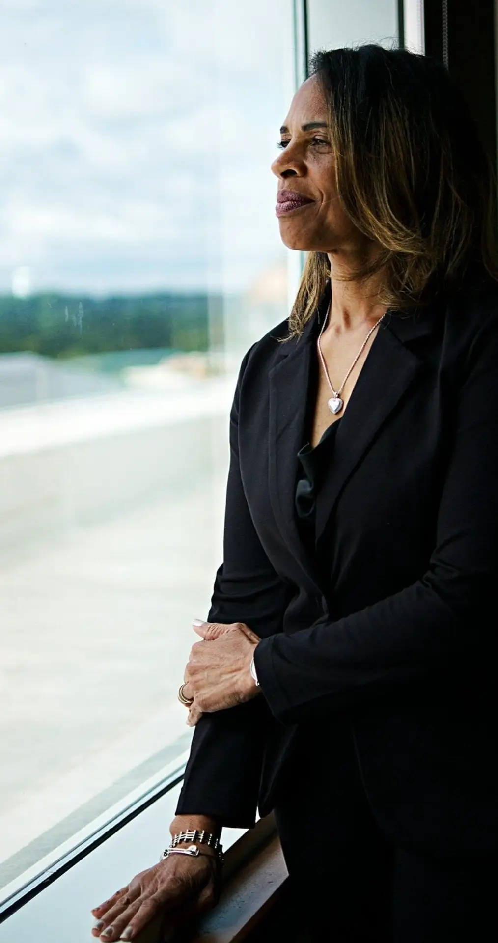 A woman in a black formal attire looking out the window smiling softly.