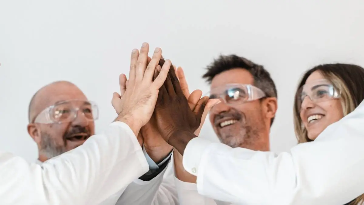 People in lab coats looking so happy and high fiving each other.