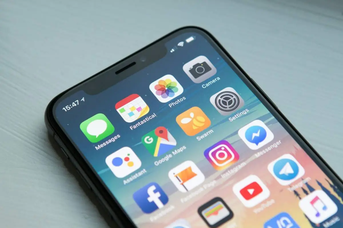 An iPhone on a white table with the homescreen open with different applications on the screen showing.