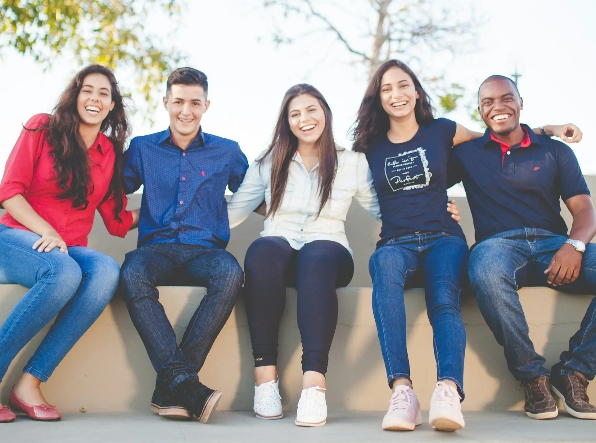 a group of people sitting next to each other on a stone wall smiling