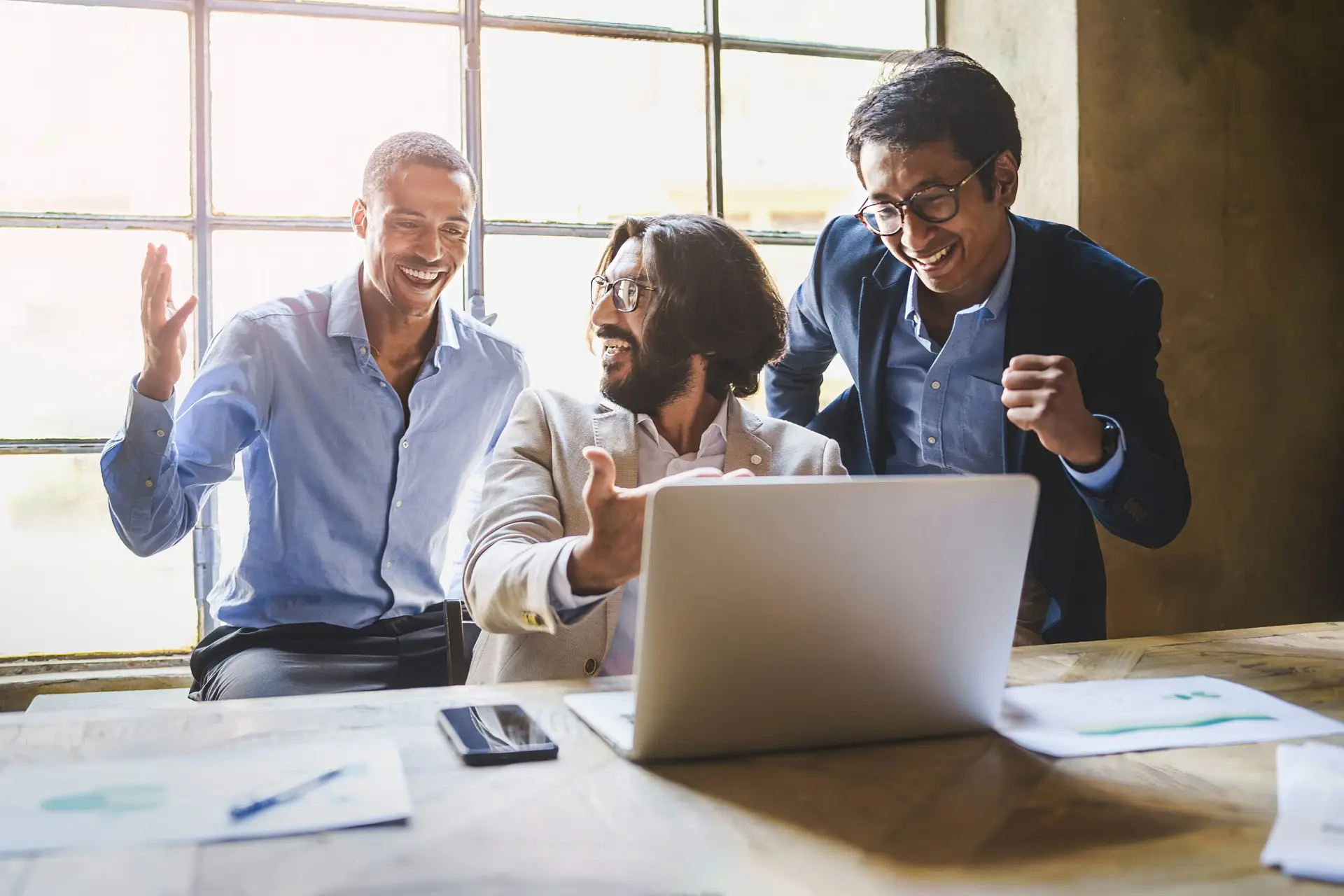 Three business professionals celebrating success with a laptop open on a wooden table.