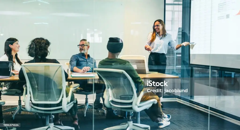a business woman presenting and smiling to other people in an office.